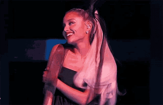 ariana grande is wearing a black dress and headphones and dancing on stage .