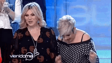 two women are standing next to each other on a stage . one of the women is wearing a polka dot shirt .