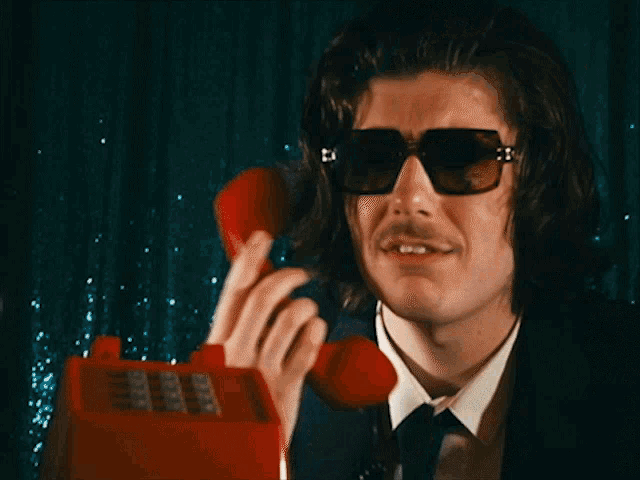 a man wearing sunglasses and a suit is holding a red telephone with the words what is wrong with you below him