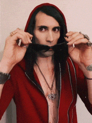 a man in a red hoodie holds sunglasses in front of his mouth