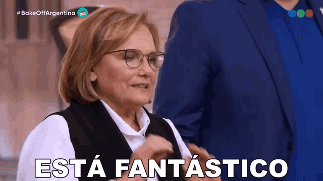 a woman with glasses says " esta fantastico " in front of a man in a suit