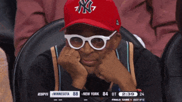 a man wearing a new york yankees hat sits in a stadium watching a game
