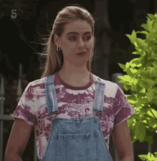 a woman wearing overalls and a tie dye shirt with the number 5 on the bottom