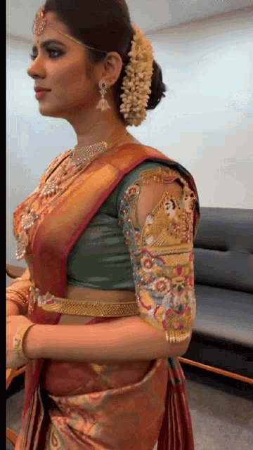 a woman wearing a green blouse and a red saree stands in front of a couch