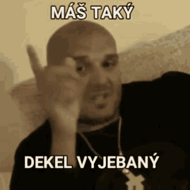 a bald man is giving the middle finger while wearing a black shirt and necklace .