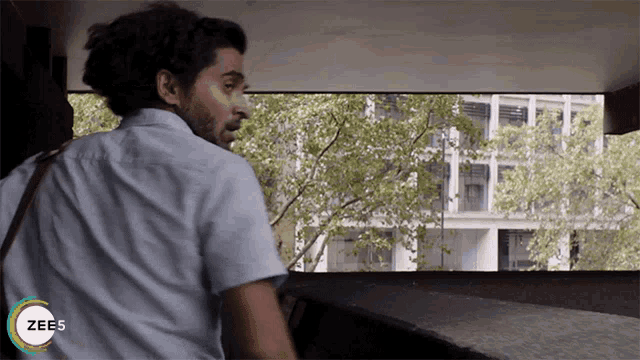 a man in a white shirt is looking out a window with the word zee5 on the bottom