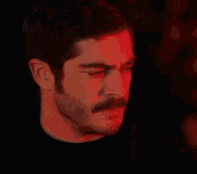 a close up of a man with a mustache in a dark room .
