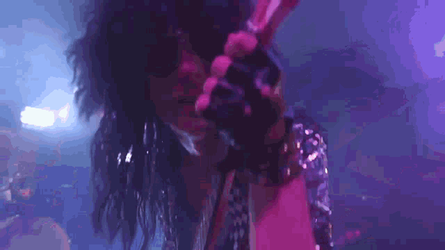 a close up of a person singing into a microphone with purple lights in the background