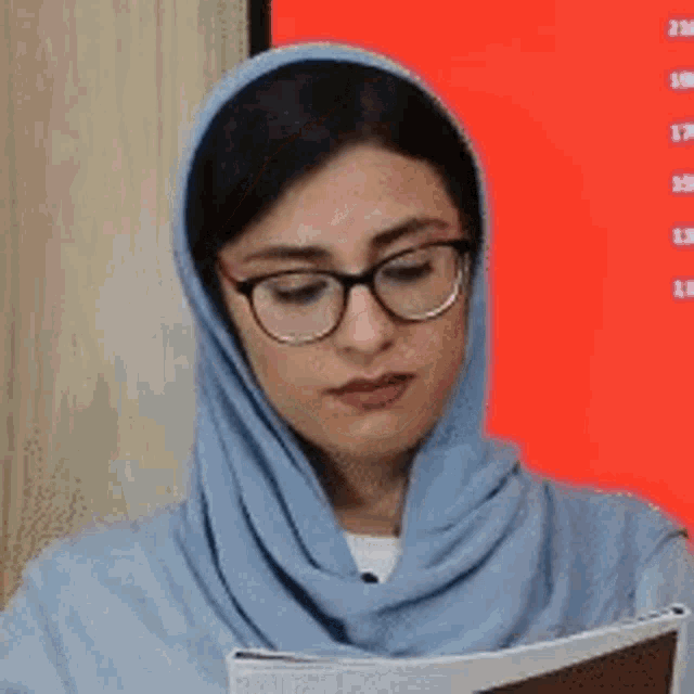 a woman wearing glasses and a scarf is reading a book