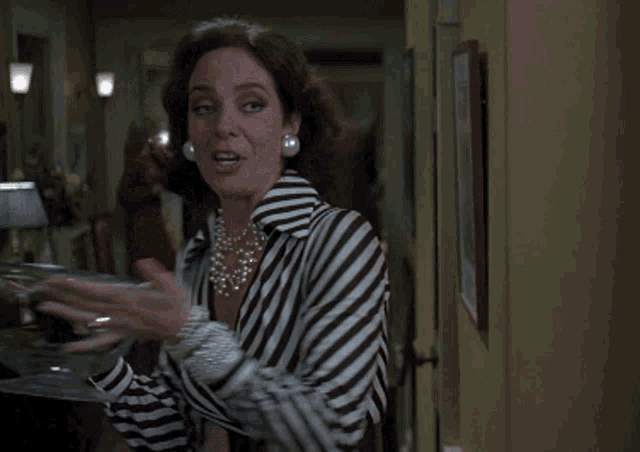 a woman in a striped shirt and pearl necklace is holding a bowl