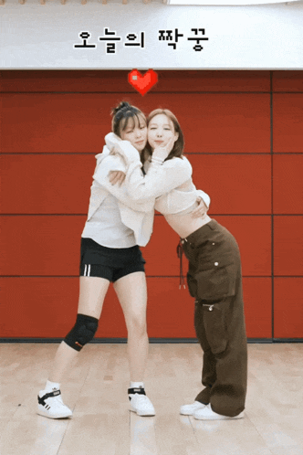two girls hugging each other in front of a sign that says ' 오늘 의 짝꿍 '