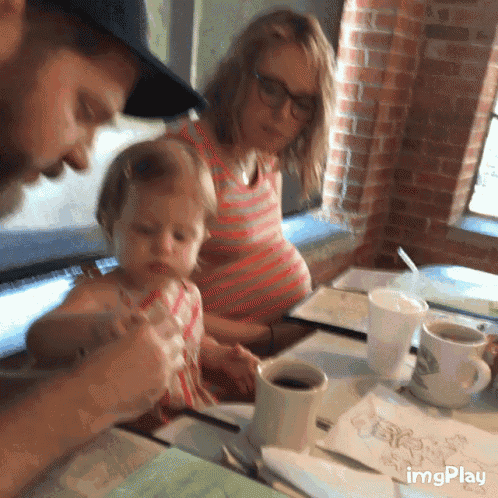 a pregnant woman sits at a table with a little girl and a man while a cup of coffee sits on the table