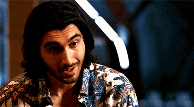 a man with long hair and a beard is wearing a floral shirt