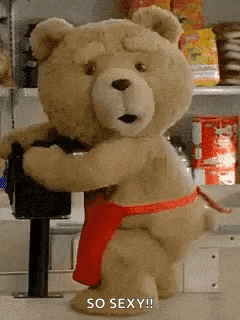 a teddy bear wearing a red apron is standing next to a machine .