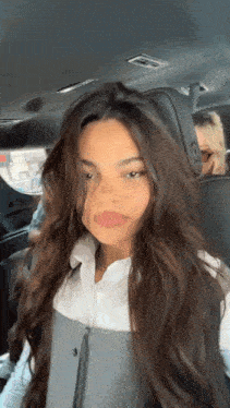 a woman with long brown hair is sitting in the back seat of a car looking at the camera .