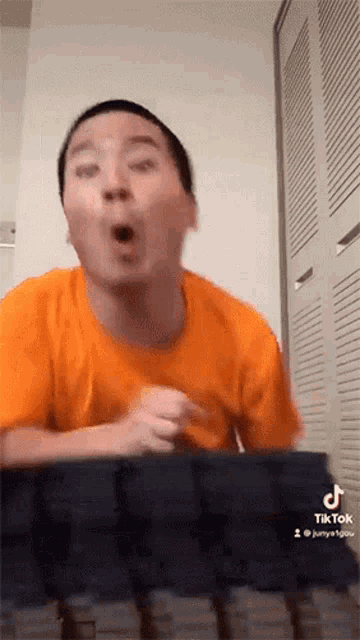 a man in an orange shirt is making a funny face while sitting at a keyboard .
