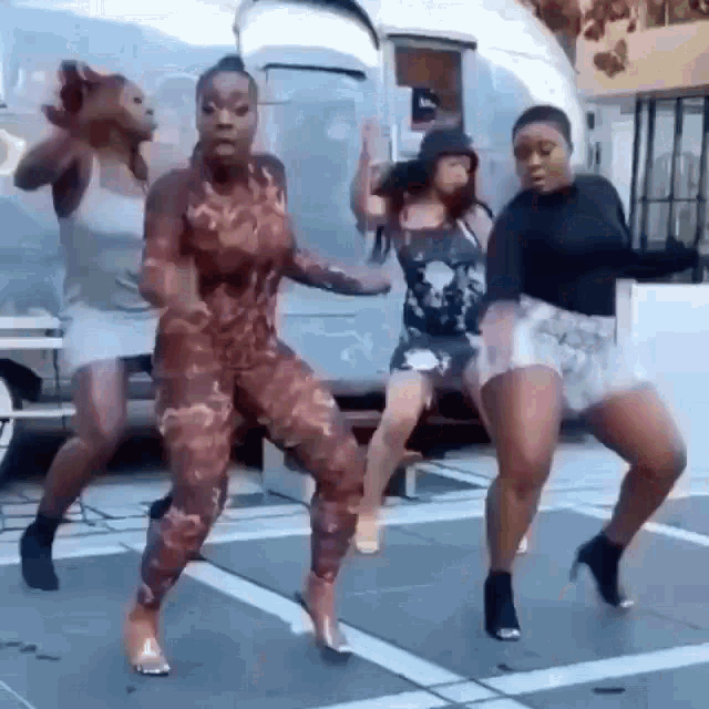 a group of women are dancing on a sidewalk in front of a trailer .