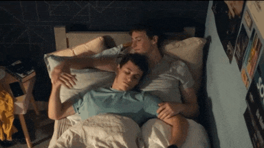 a couple of men laying in bed with posters on the wall including one that says so