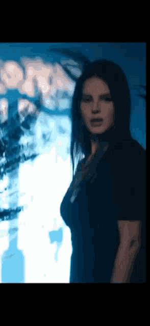a woman in a black dress is standing in front of a blue wall