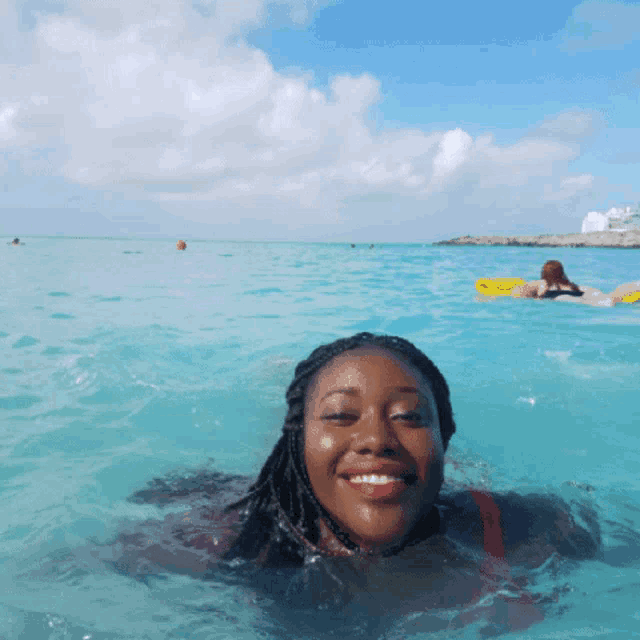 a woman is swimming in the ocean with a yellow raft in the background