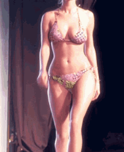 a woman in a bikini is walking on a stage in front of a curtain .