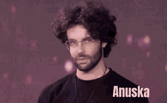 a man with curly hair and glasses is wearing a black shirt that says anuska on it