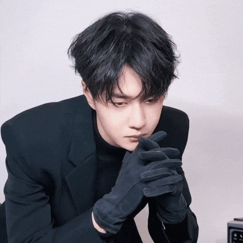 a young man wearing black gloves and a black suit