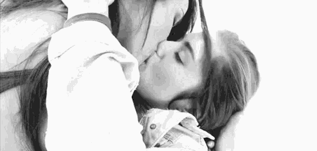 a black and white photo of two women kissing each other on a bed .