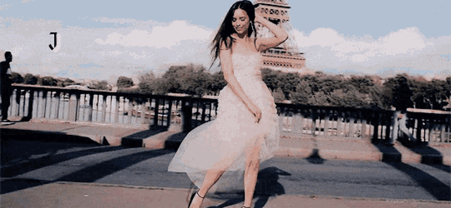 a woman in a pink dress is dancing on a bridge with the letter j in the corner