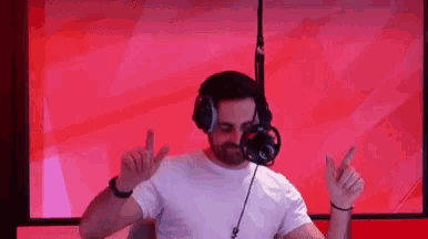 a man wearing headphones and a white shirt is dancing in front of a red background .