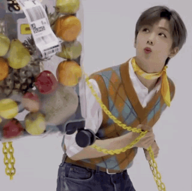 a man wearing a vest and a scarf is standing in front of a container of fruit .
