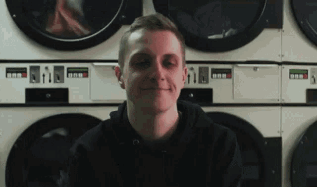 a man is sitting in a laundromat surrounded by washing machines .