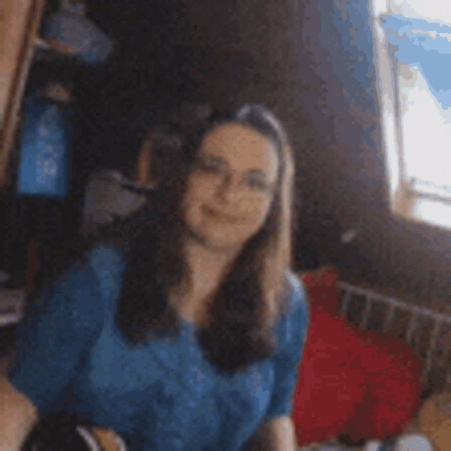a woman wearing glasses and a blue shirt is clapping her hands in front of a window .