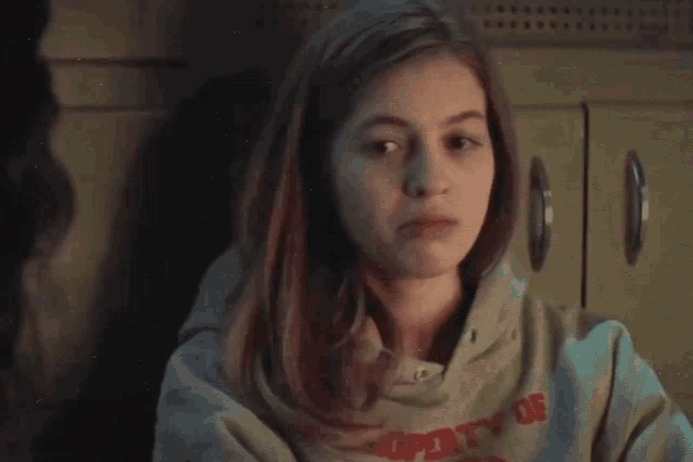 a young girl wearing a sweatshirt that says property of is sitting in front of a cabinet .