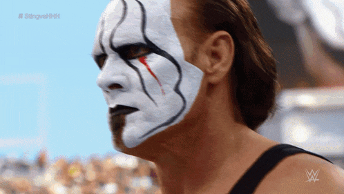 a man with a white face paint and a wrestling logo on his arm