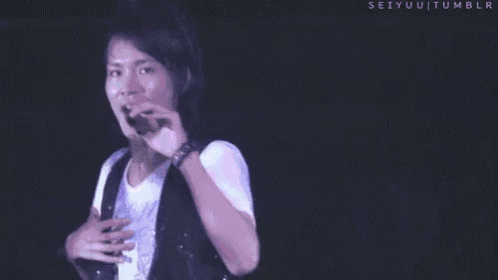 a man in a white shirt is singing into a microphone on a stage in front of a crowd .