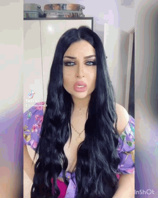 a woman with long black hair is wearing a purple top and a gold necklace