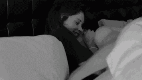 a black and white photo of a man and woman laying in bed holding hands .
