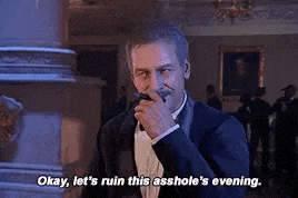 a man in a tuxedo is talking into a microphone in a room while holding a cigar .