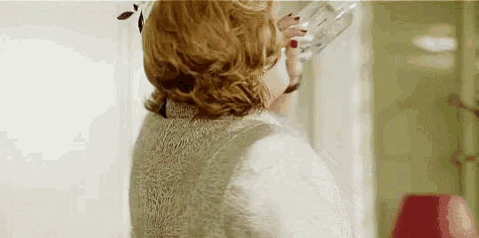 a woman is drinking a glass of water from a bottle in a room .