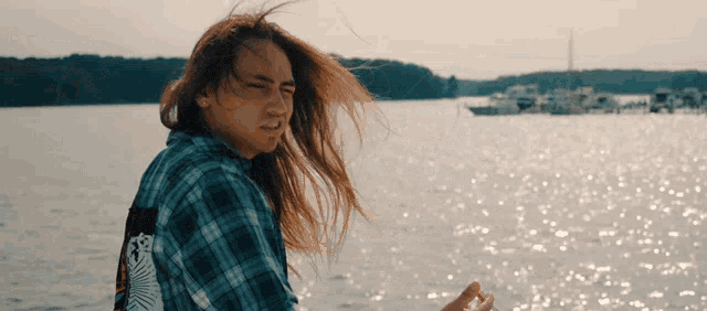 a woman in a plaid shirt is standing in front of the water