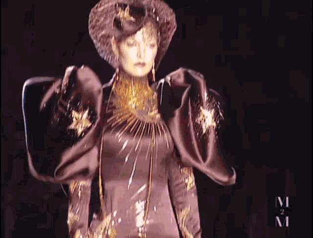 a woman is walking down a runway wearing a hat and a necklace ..
