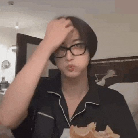 a man wearing glasses is eating a donut and scratching his forehead .