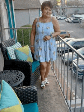 a woman in a blue dress is standing on a balcony next to chairs .