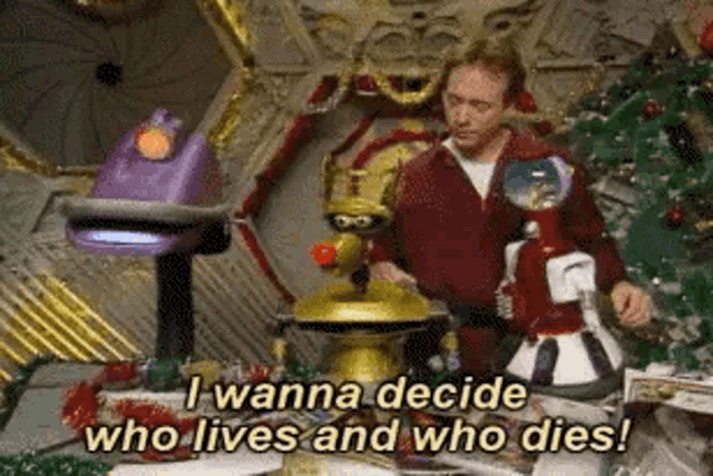 a man is standing in front of a christmas tree with robots and says `` i wanna decide who lives and who dies '' .