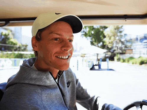 a man wearing a white nike hat and a grey hoodie smiles
