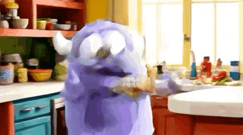 a purple monster with horns is standing in a kitchen eating a piece of food .
