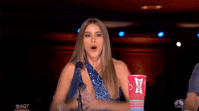 a woman in a blue dress stands in front of a microphone next to a cup that says sonic on it