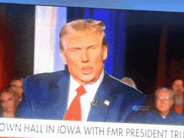 a tv screen shows a man in a suit and tie with the words own hall in iowa with fmr president tru on it