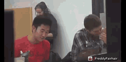 a man in a red shirt is sitting at a desk with a laptop ..